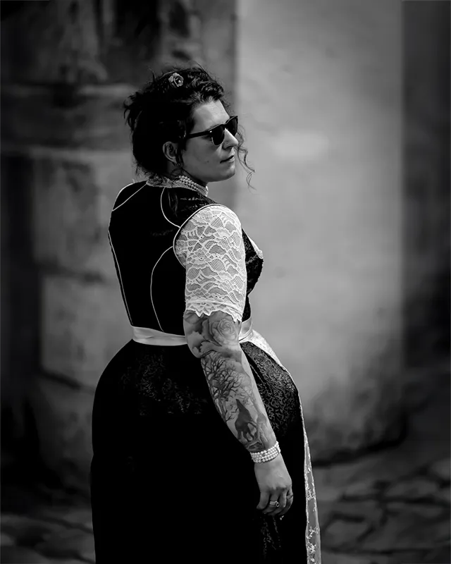 Schwarzweiß-Porträt einer tätowierten Frau mit Sonnenbrille und traditionellem Kleid