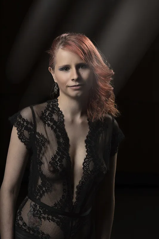 Studio-Porträt einer Frau mit rötlichem Haar in schwarzem Spitzenoutfit vor dunklem Hintergrund