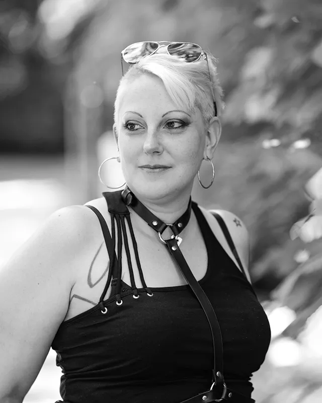 Schwarz-Weiß-Porträt einer Frau mit kurzem Haar, Sonnenbrille und schwarzem Oberteil im Freien.